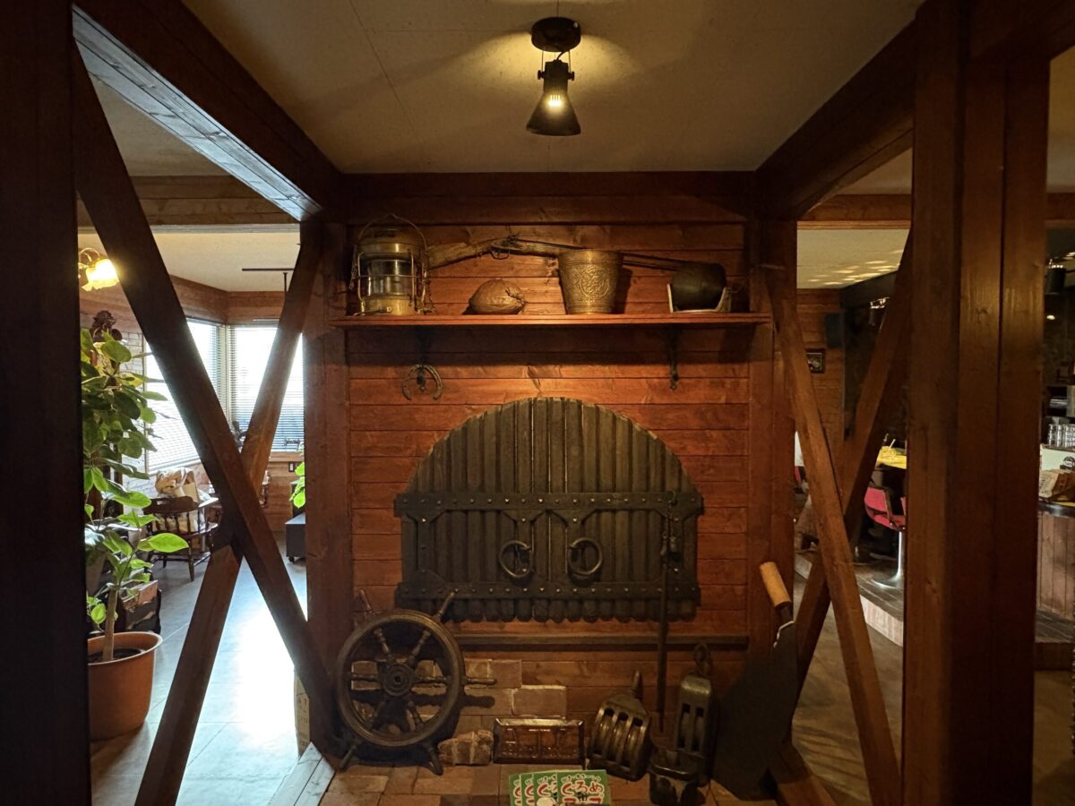 網走「珈琲屋 デリカップ」の店内ディスプレイ。ウッド調の壁に船の舵やアンティークなランプ、ヴィンテージの小物が飾られ、隠れ家のような落ち着いた空間を演出している。
Interior decorations of "Coffee-ya Delicup" in Abashiri, featuring nautical antiques like a ship's wheel and vintage lamps against warm wooden walls.