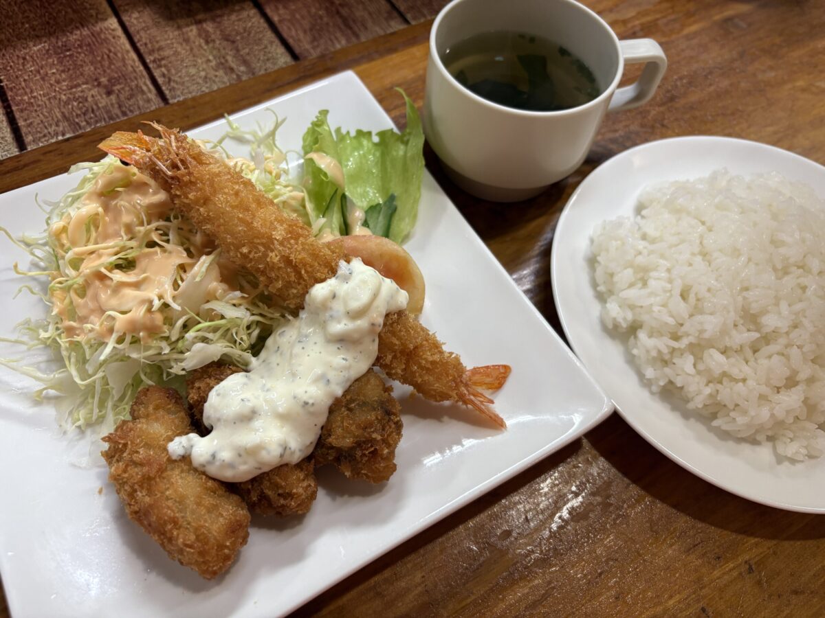 網走「レストラン ホワイトハウス」のエビフライとカキフライの定食。タルタルソースがたっぷりかかった大きなエビフライとサクサクのカキフライに、山盛りのキャベツ、ライス、スープが添えられている。
A set meal of deep-fried shrimp and oysters at "Restaurant White House" in Abashiri, served with tartar sauce, fresh cabbage, rice, and soup.