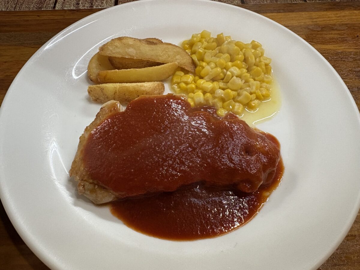 網走「レストラン ホワイトハウス」の肉料理。厚切りの肉に特製の赤いソースがたっぷりとかかり、付け合わせにコーンソテーとフライドポテトが添えられた、ボリューム満点の一皿。
A hearty meat dish at "Restaurant White House" in Abashiri, featuring a thick steak topped with rich red sauce, served with sautéed corn and fried potatoes.