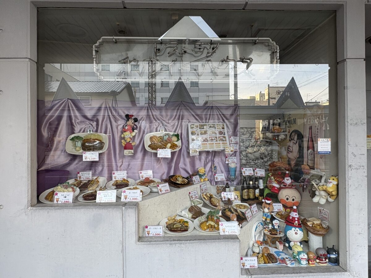 網走「レストラン ホワイトハウス」店頭の大きなショーウインドー。ステーキ、ハンバーグ、海鮮丼、デザートなど、色鮮やかでボリューム満点な食品サンプルが所狭しと並んでいる。
A large display window at "Restaurant White House" in Abashiri, filled with realistic food samples of steaks, seafood bowls, and desserts.