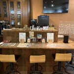 「UROKO」の広々としたカウンター席。オープンキッチンの前にはゆったりとした椅子が並び、高い天井と開放的な空間が特徴。夜にはバーのような雰囲気も楽しめそうな、洗練された内装。 The spacious counter seating area at "UROKO" in Abashiri. Features comfortable chairs lined up in front of the open kitchen, with high ceilings creating an airy and sophisticated atmosphere.