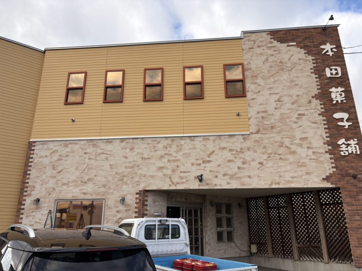 網走市にある老舗菓子店「本田菓子舗」の建物外観。明るいベージュとレンガ調の壁面が特徴的で、右側には大きく「本田菓子舗」の文字が掲げられている。
The exterior of Honda Kashiho, a long-established confectionery shop in Abashiri. The building features a warm beige and brick-patterned facade with the shop's name written in Japanese.
