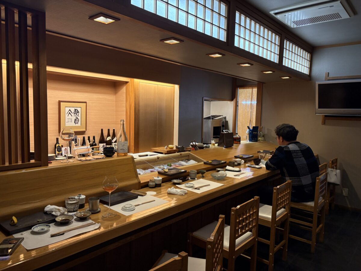 網走「鮨 やまし田」の店内。美しく磨かれた白木のカウンターが広がり、落ち着いた和の照明が上質な空間を演出している。職人の技を目の前で楽しみながら、網走の旬を味わえる特等席の様子。
The interior of Sushi Yamashita in Abashiri, featuring a beautiful polished wooden counter and warm, ambient lighting. The shot captures the sophisticated and serene atmosphere of a high-end Japanese sushi bar.