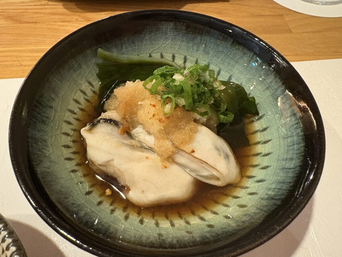 網走「鮨 やまし田」で提供されたオホーツク産の大きな生牡蠣。殻に盛り付けられたふっくらと瑞々しい牡蠣の身に、爽やかな薬味が添えられた、素材の良さが際立つ一皿。
A large, fresh Okhotsk oyster served at Sushi Yamashita in Abashiri. The plump and succulent raw oyster is elegantly presented in its shell with delicate garnishes, highlighting the premium quality of local seafood.