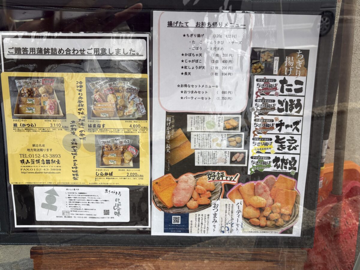 網走「横山蒲鉾店」の店頭に掲示されたメニュー。たこ、ごぼう、チーズなどの「ちぎり揚げ」や「かぼちゃ天」などの単品メニューのほか、地方発送可能な贈答用の蒲鉾詰め合わせセット（桂、はまなす、しらかば）が紹介されている。
The shop menu for Yokoyama Kamaboko in Abashiri, listing various freshly fried fish cakes like octopus, burdock, and cheese flavors. It also features several gift assortment sets available for shipping nationwide.