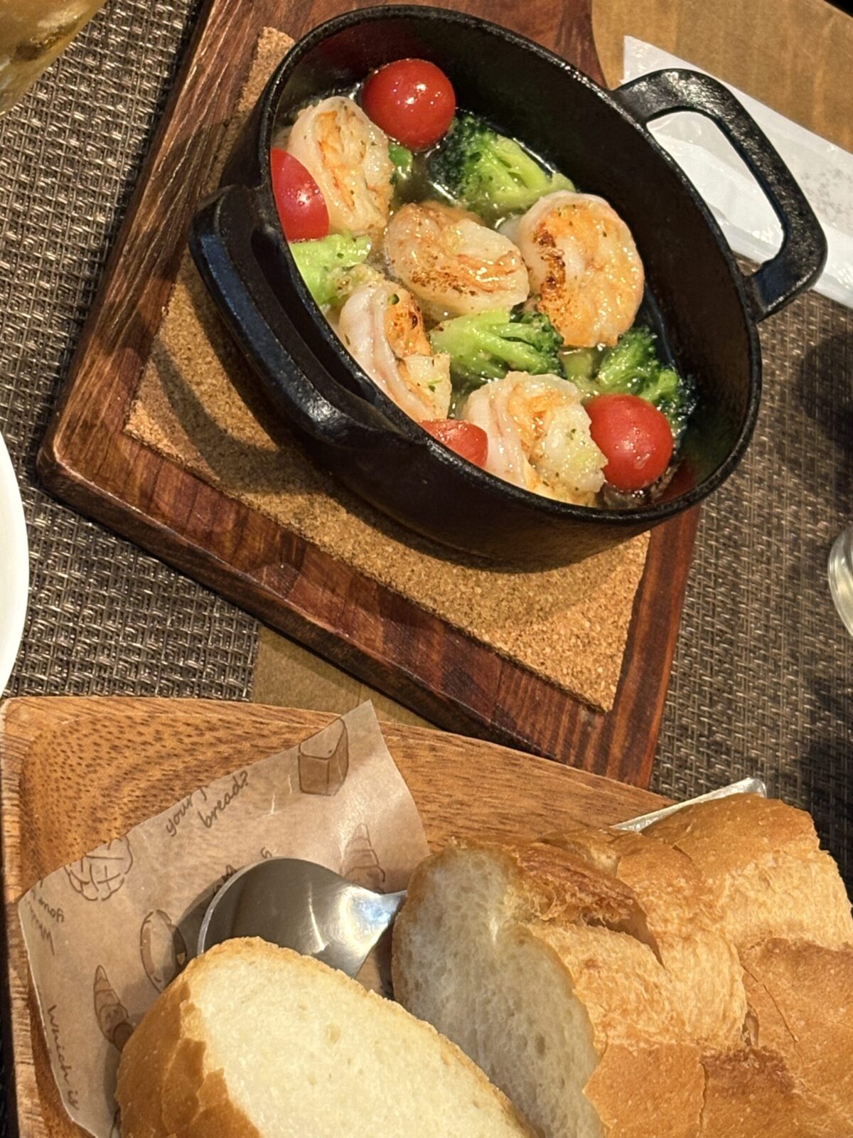 網走「キッチンウロコ」のエビとブロッコリーのアヒージョ。スキレットで熱々に仕上げた一皿と、香ばしく焼かれたバゲットのセット
Sizzling shrimp and broccoli ajillo served with toasted baguette slices at OsteriaBAR UROKO in Abashiri.