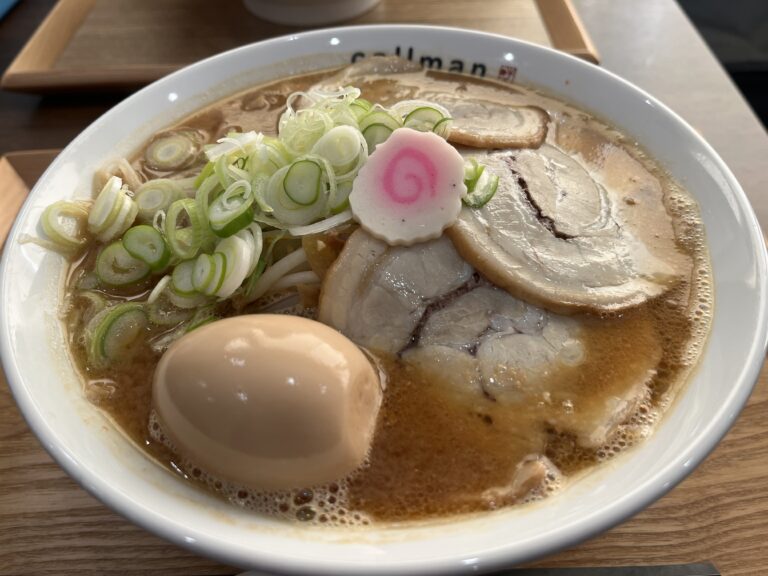 網走市の「らー麺 こーるまん」で提供される「コールマン味噌ラーメン」。濃厚そうな味噌スープに、大ぶりのロールチャーシュー3枚、丸ごとの味付け玉子、たっぷりの刻みネギ、メンマ、そしてピンクの渦巻き模様のナルトがトッピングされている。白い丼には「callman」のロゴが見える。 A hearty bowl of "Callman Miso Ramen" from "Ramen Callman" in Abashiri, Hokkaido. The rich miso-based broth is topped with three large slices of rolled chashu pork, a whole soft-boiled seasoned egg, abundant finely sliced green onions, bamboo shoots (menma), and a classic pink-and-white fish cake (naruto). The white bowl has the restaurant's logo "callman" printed on it.