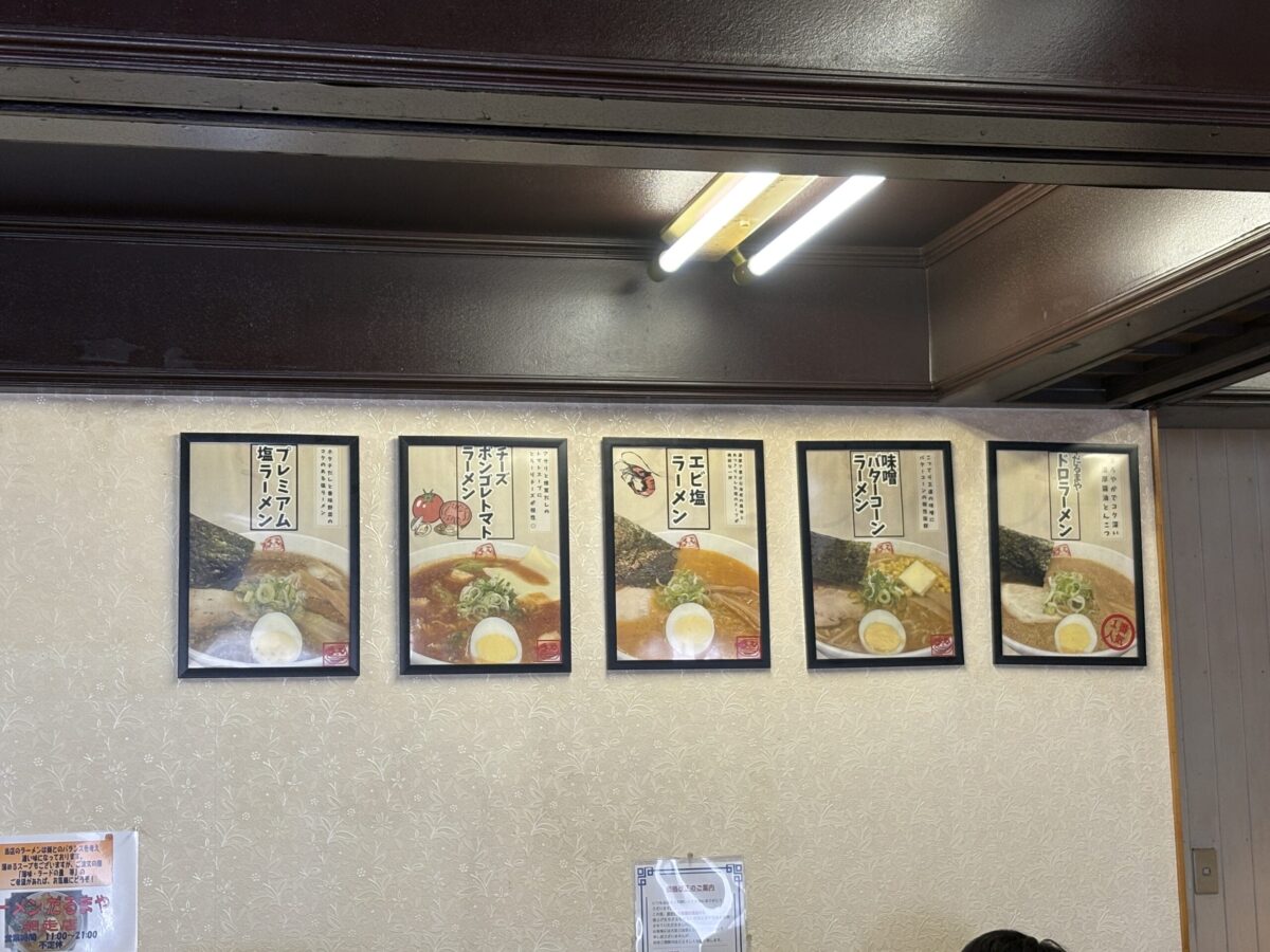 店内の壁に掲示された「だるまや」の人気メニューパネル。左からプレミアム塩ラーメン、チーズボンゴレトマトラーメン、エビ塩ラーメン、味噌バターコーンラーメン、そして一番人気のドロラーメンが写真付きで紹介されている。
Menu panels on the wall at Ramen Darumaya, showcasing colorful photos of their dishes: Premium Salt, Cheese Vongole Tomato, Shrimp Salt, Miso Butter Corn, and the most popular "Doro Ramen."