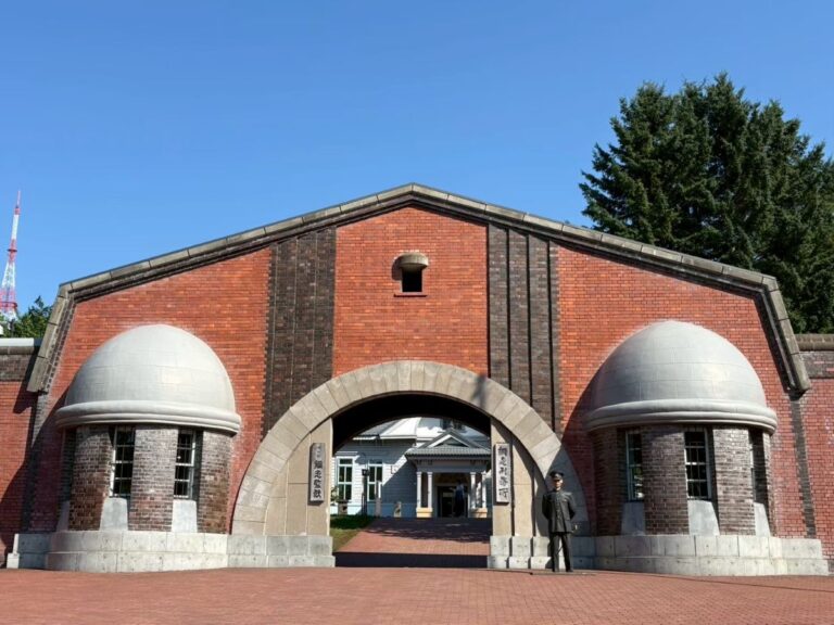 博物館 網走監獄の赤煉瓦正門。門の前に立つ看守のマネキン人形が当時の雰囲気を再現 Full view of the Abashiri Prison Museum main gate with a realistic guard figure standing at the entrance.