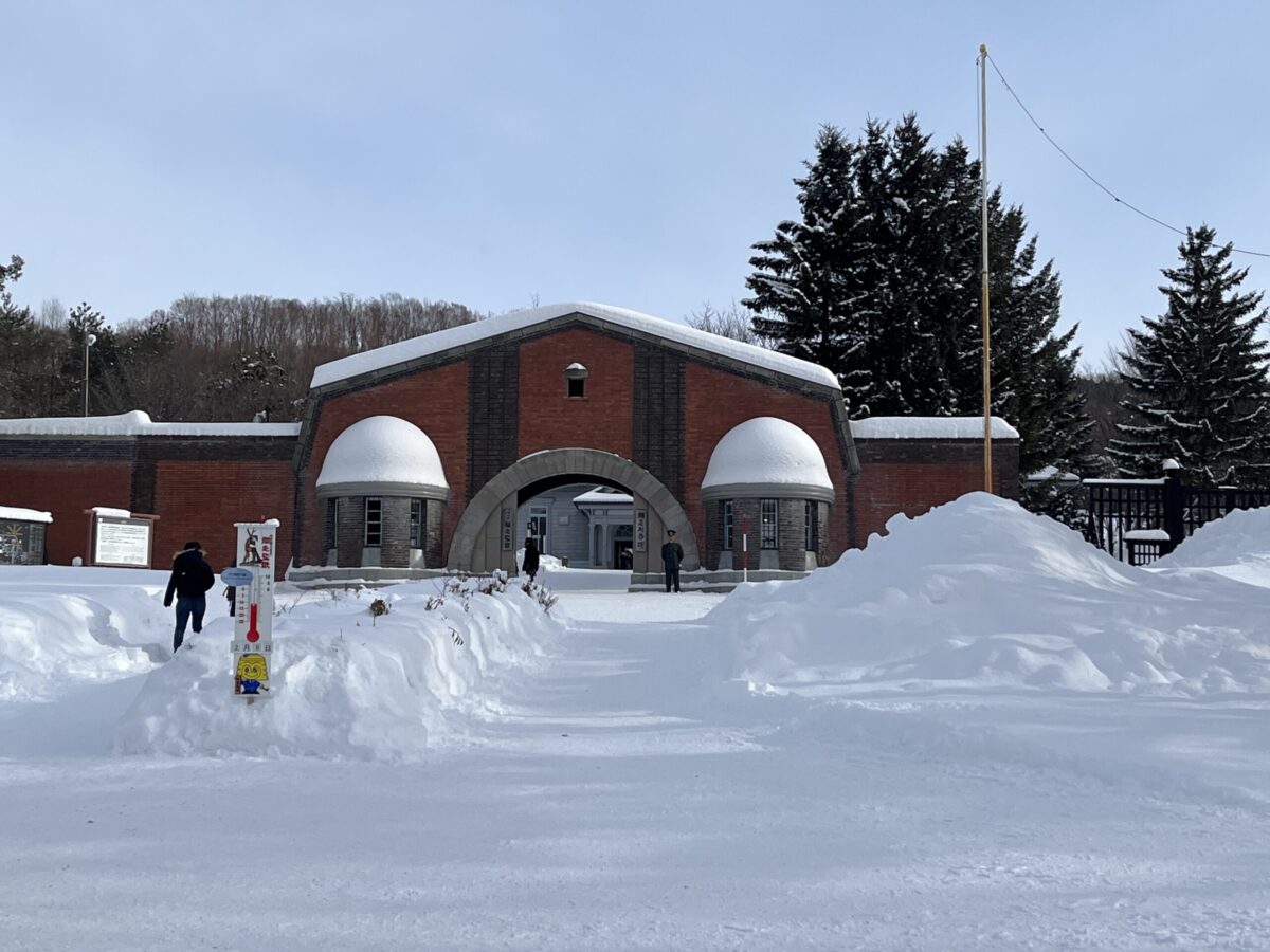 雪が積もった冬の網走監獄正門（赤煉瓦門）。手前には網走の気温を示す温度計がある風景