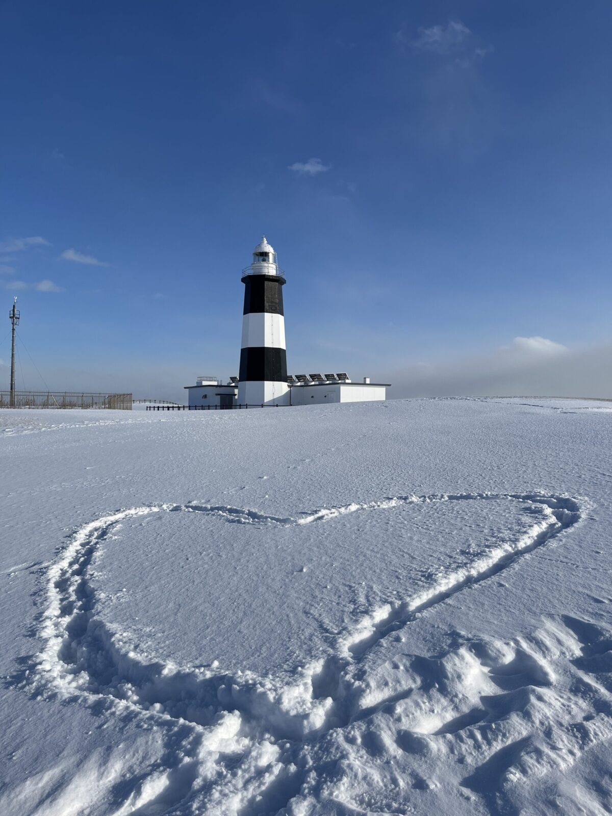 雪に覆われた能取岬灯台と、雪原に描かれた大きなハートの足跡