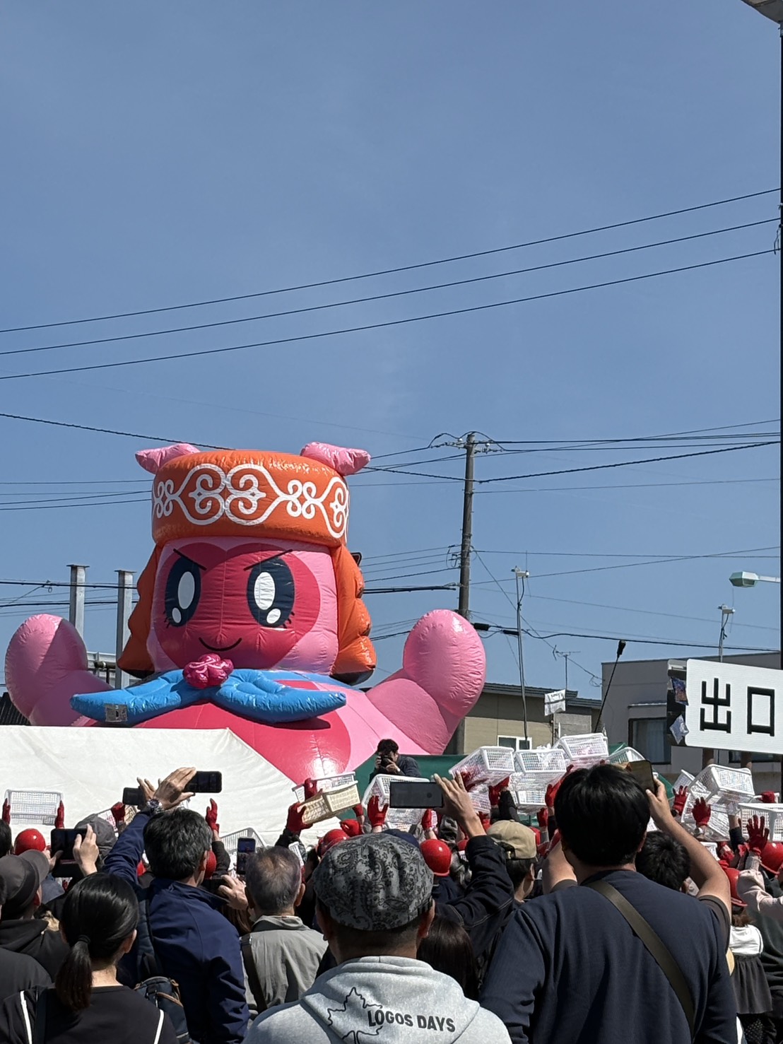 春カニ合戦in網走のステージ前で、白いカゴやスマホを掲げてイベントを楽しむ大勢の観客とニポネバルーン