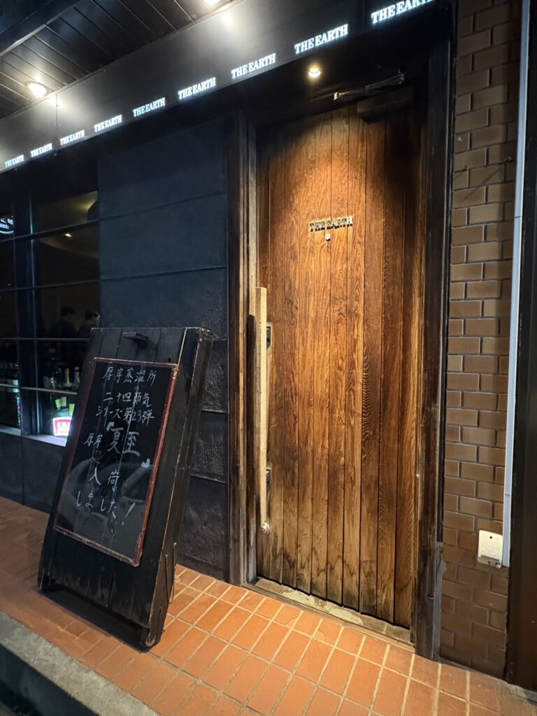 網走の本格派バー「BAR THE EARTH（ジアス）」の重厚な木製の扉と看板の外観 Wooden entrance door and illuminated sign of BAR THE EARTH, a bar in Abashiri, Hokkaido.