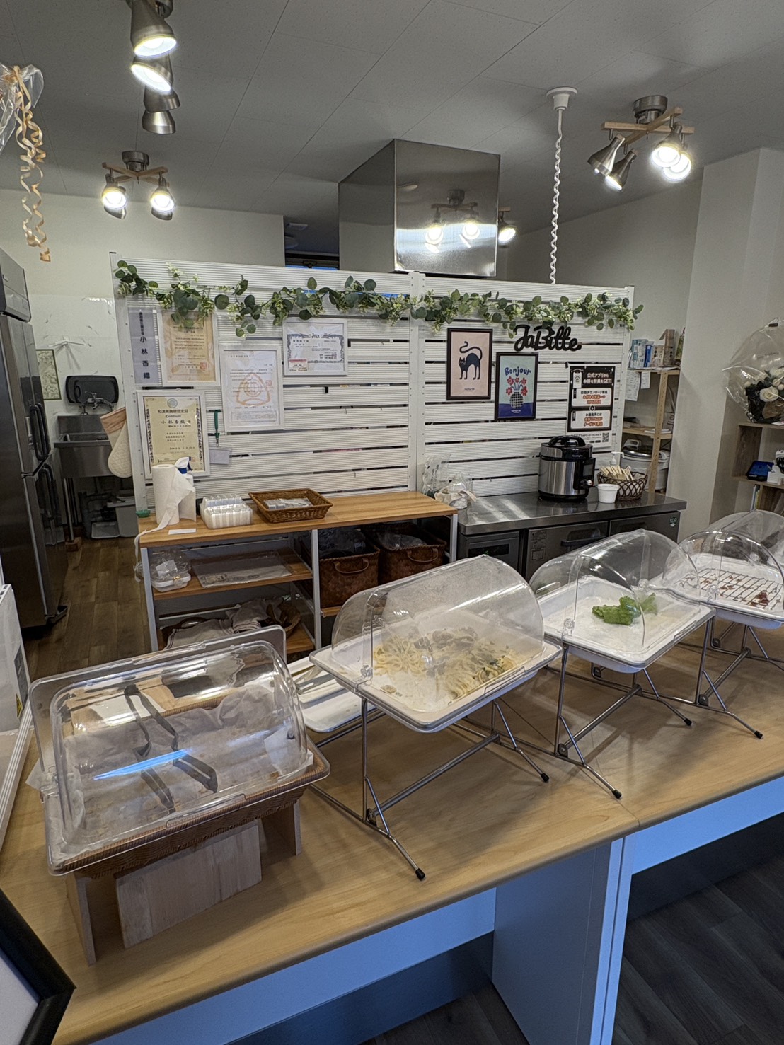 白を基調とした清潔感のある「ja.bitte（ビッテ）」の店内とお惣菜が並ぶカウンターデリ
Clean and white-themed interior of ja.bitte with a variety of handmade deli dishes on the counter.