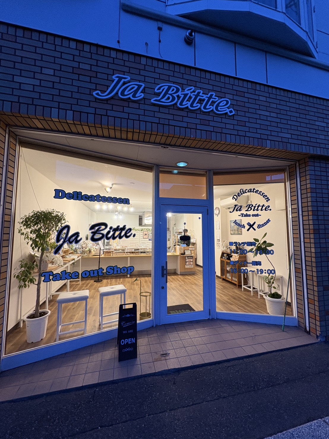 網走のデリカテッセン「ja.bitte（ビッテ）」のガラス張りでおしゃれな店舗外観夜のライトアップ）
Stylish glass storefront of delicatessen ja.bitte in Abashiri at night with warm lighting.