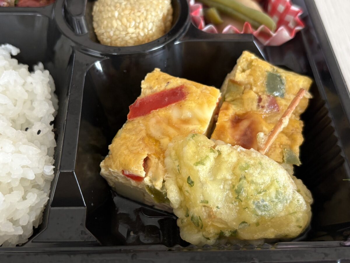 網走「ja.bitte（ビッテ）」のお弁当に入る、パプリカやピーマンが鮮やかな厚焼き卵（スパニッシュオムレツ風）と胡麻団子のアップ
Close-up of a colorful Spanish-style omelet with bell peppers and a sweet sesame ball in ja.bitte's bento box.