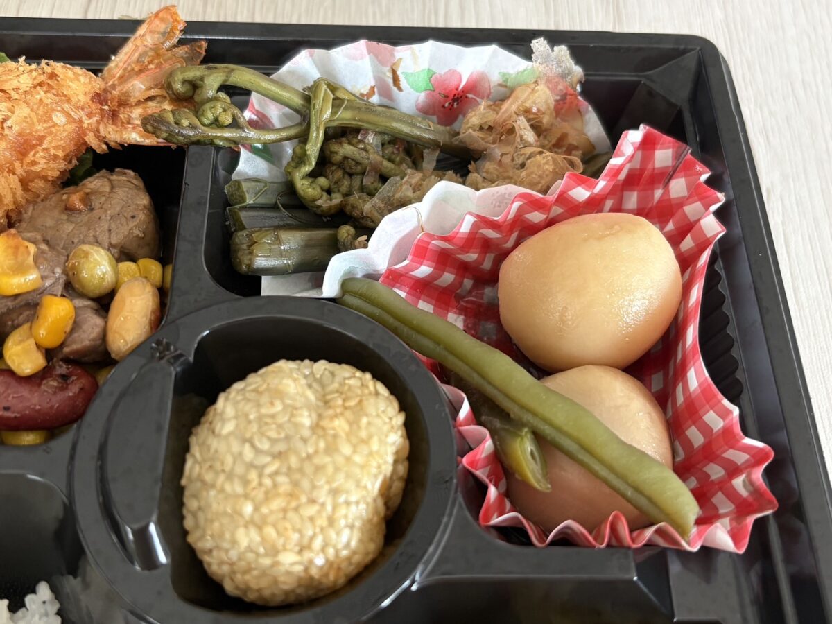 「ja.bitte（ビッテ）」のお弁当の副菜、網走周辺の旬の山菜こごみのおひたしと小玉ねぎの煮物
Close-up of seasonal wild vegetable "Kogomi" and simmered onions as side dishes in the bento box.