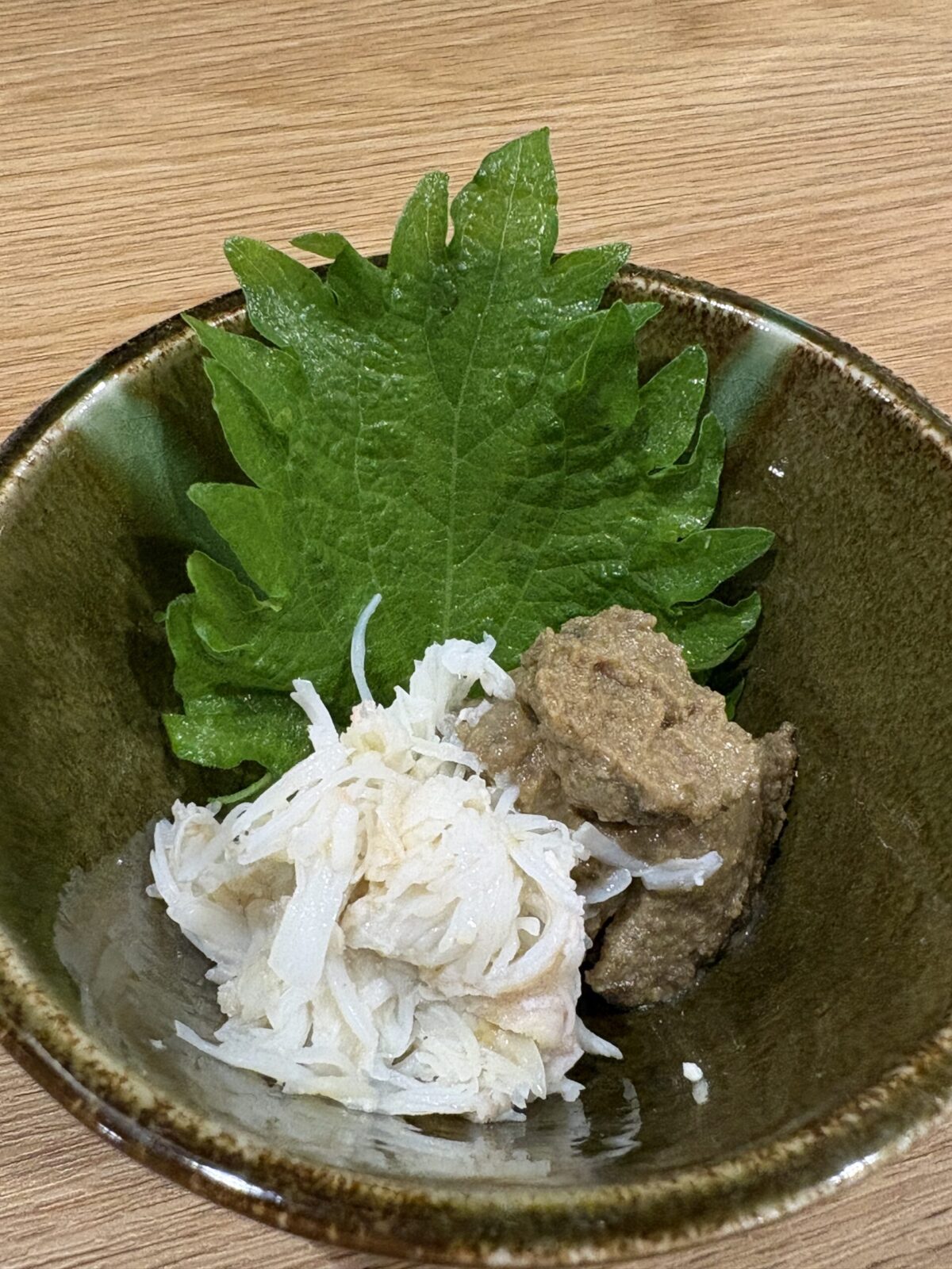 網走「なかの酒場」の小鉢に盛られた、ほぐしたカニの身と濃厚なカニ味噌（ズワイガニのみそ）に大葉を添えた一皿
Rich snow crab paste mixed with shredded crab meat (Kani Miso) served in a small bowl with a shiso leaf at Nakano Sakaba in Abashiri.