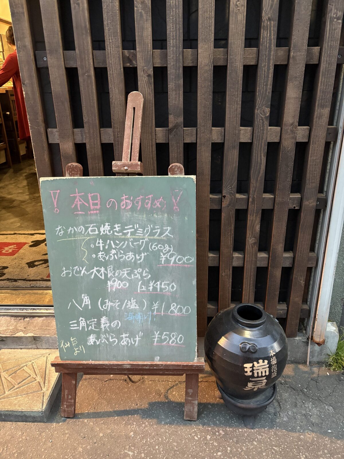 網走「なかの酒場」の店外に設置された、「本日のおすすめ」が手書きされた緑色の黒板スタンド。八角や石焼きデミグラスなどが並ぶ
A green chalkboard menu stand outside Nakano Sakaba in Abashiri, showing handwritten daily specials including Hakkaku fish.