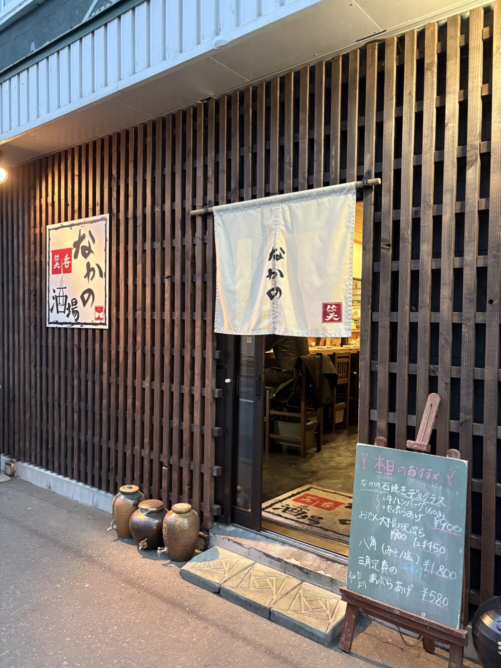 夜の照明に優しく照らされた、網走の大衆酒場「なかの酒場」の風情ある店舗外観と入り口の佇まい Complete night view of the welcoming storefront and entrance of the izakaya Nakano Sakaba in Abashiri.