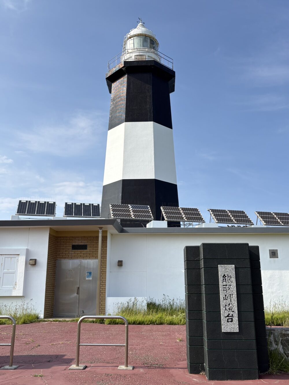 青空の下に佇む白黒のモノトーンカラーが特徴的な能取岬灯台と名称の石碑 The iconic black and white Notoro Cape Lighthouse and stone monument under a clear blue sky