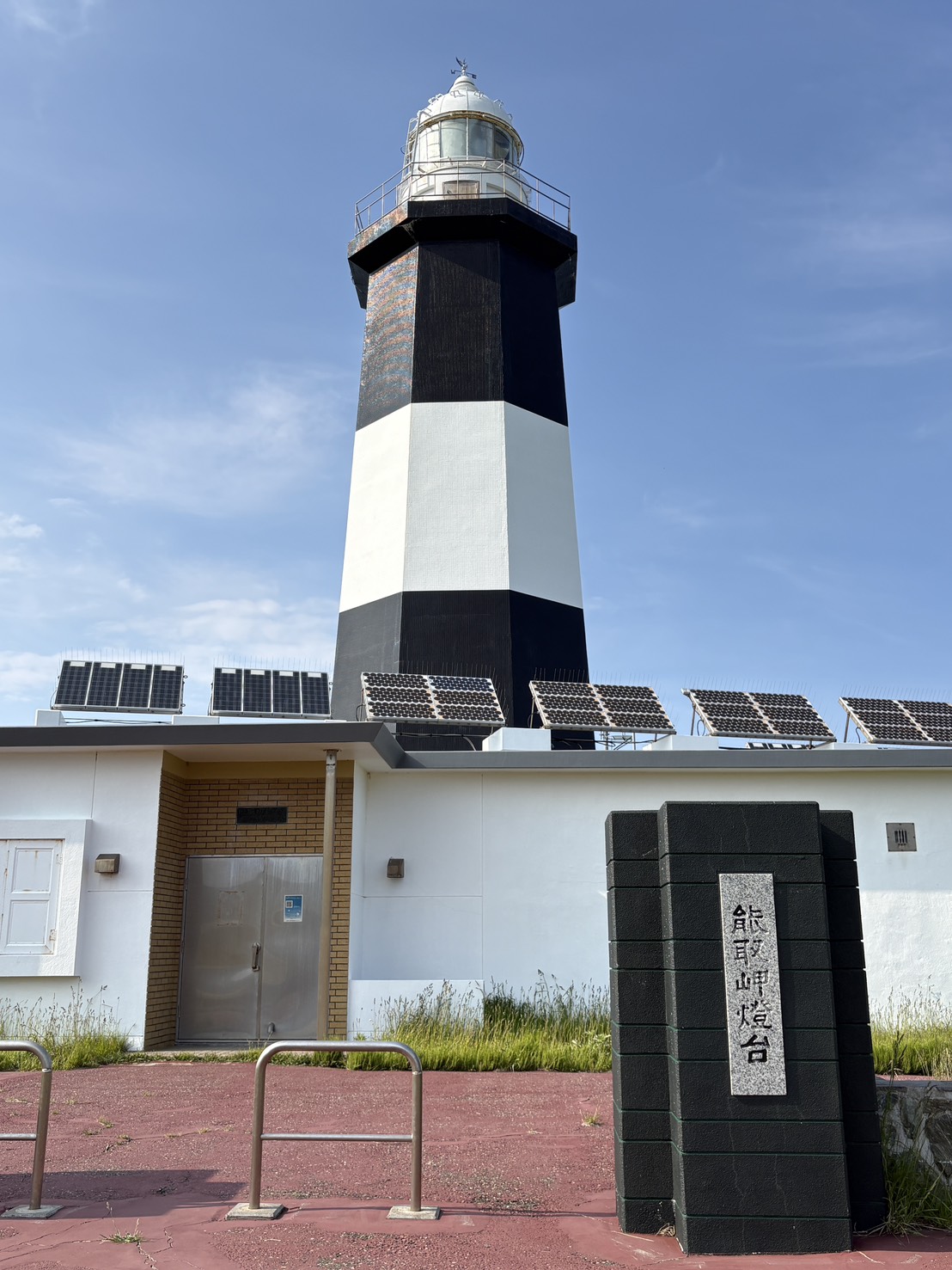 青空の下に佇む白黒のモノトーンカラーが特徴的な能取岬灯台と名称の石碑 The iconic black and white Notoro Cape Lighthouse and stone monument under a clear blue sky