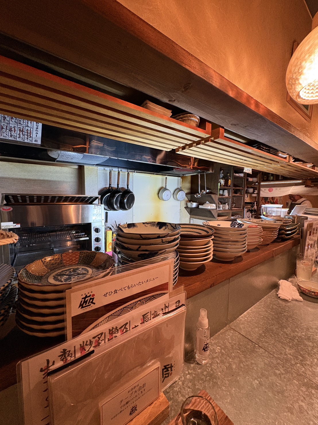 居酒屋「屯屯(TONTON)」のアットホームなカウンター席と大皿料理が並ぶ厨房の様子。
Cozy counter seating area and kitchen display with large serving dishes at izakaya TONTON in Abashiri.