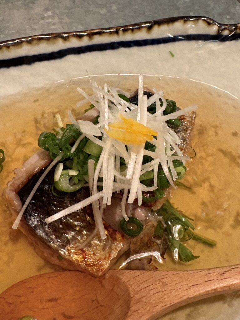 居酒屋「屯屯（TONTON）」の名物・本日の魚の焼きびたし。極上海鮮出汁と薬味、柚子皮添え。 Grilled fish in rich dashi broth topped with green onions and citrus peel at izakaya TONTON.