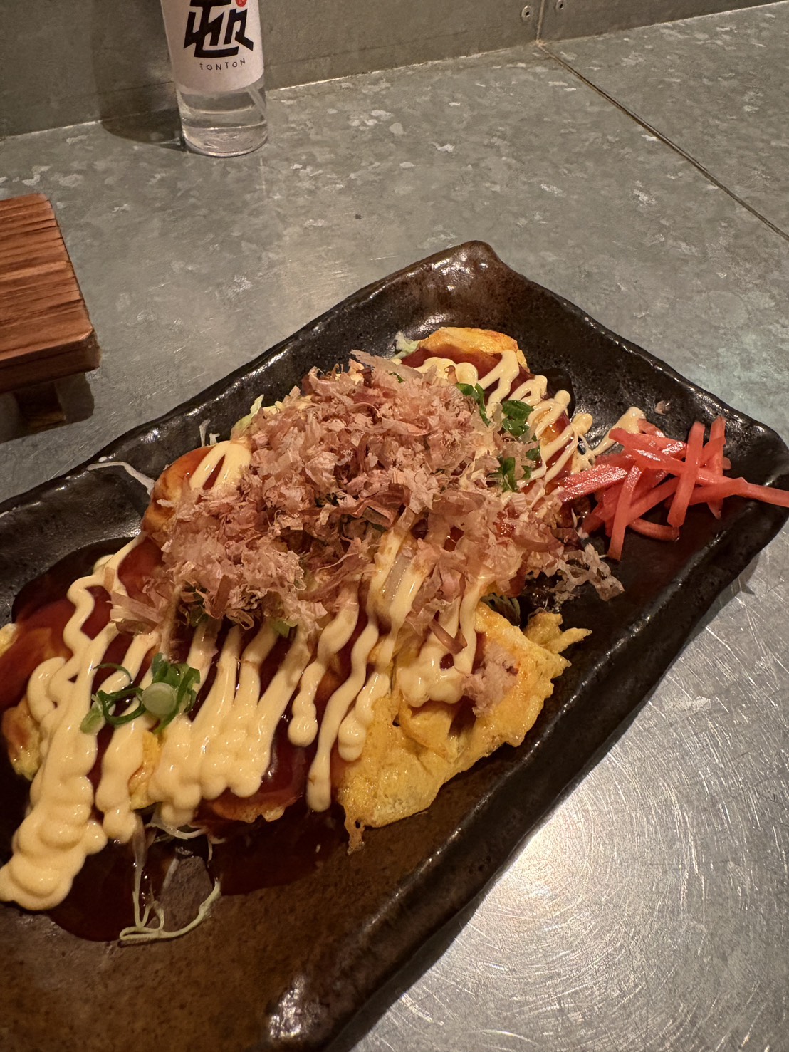 居酒屋「屯屯(TONTON)」のタコ玉焼き。マヨネーズとソース、削り節がたっぷりかかった人気メニュー。
Octopus egg pancake topped with mayonnaise, savory sauce, and bonito flakes at izakaya TONTON.