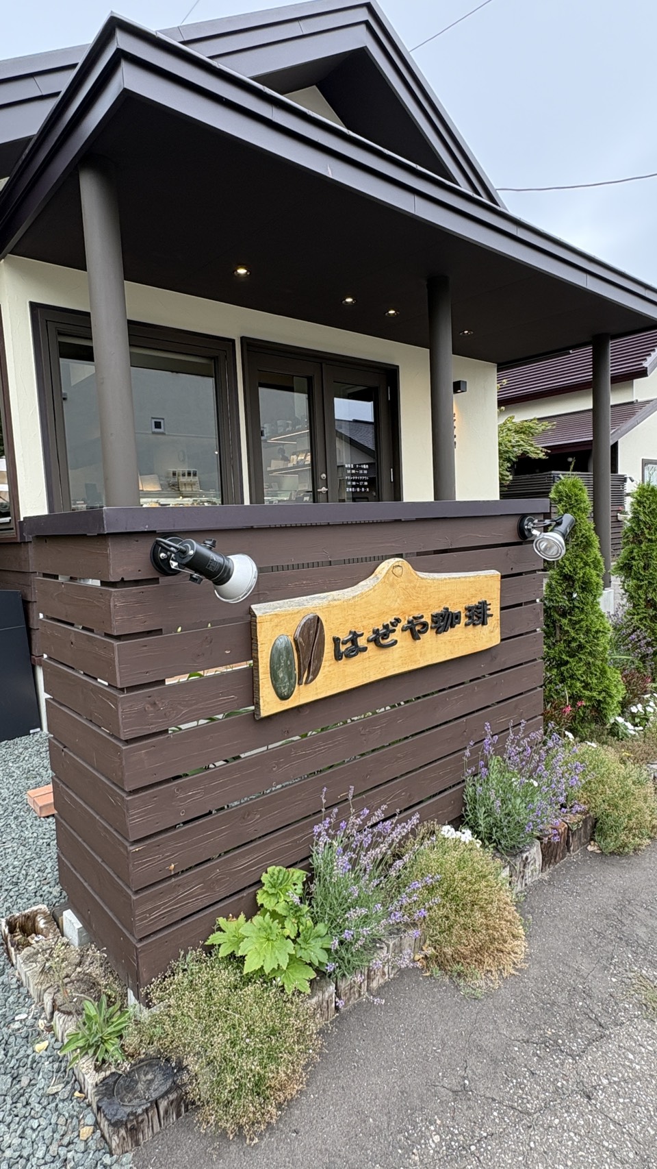 コーヒー豆のモチーフがあしらわれた「はぜや珈琲」の温かみのある木製看板と美しい花々
Wooden signboard of Hazeya Coffee featuring coffee bean motifs surrounded by flowers