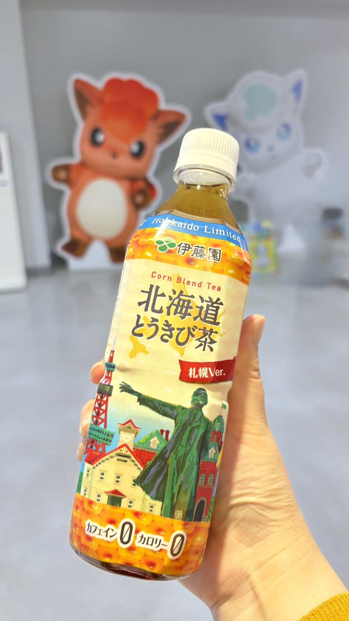 女満別空港のロビーで手に持った北海道限定の伊藤園「北海道とうきび茶」と背景のロコンのパネル
Holding a bottle of Hokkaido limited corn tea with Vulpix display in the background at Memanbetsu Airport