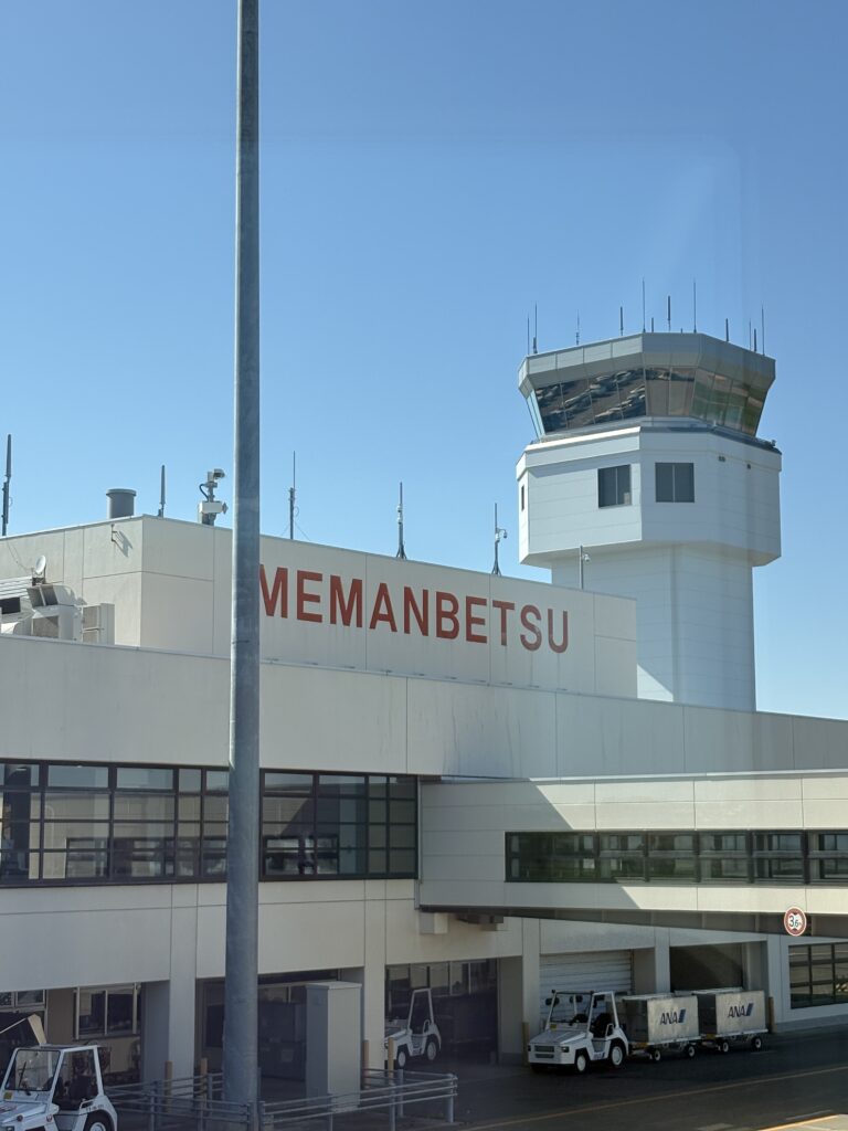 青空の下にそびえ立つ女満別空港の管制塔と「MEMANBETSU」のロゴ Memanbetsu Airport control tower and building under a clear blue sky in Hokkaido