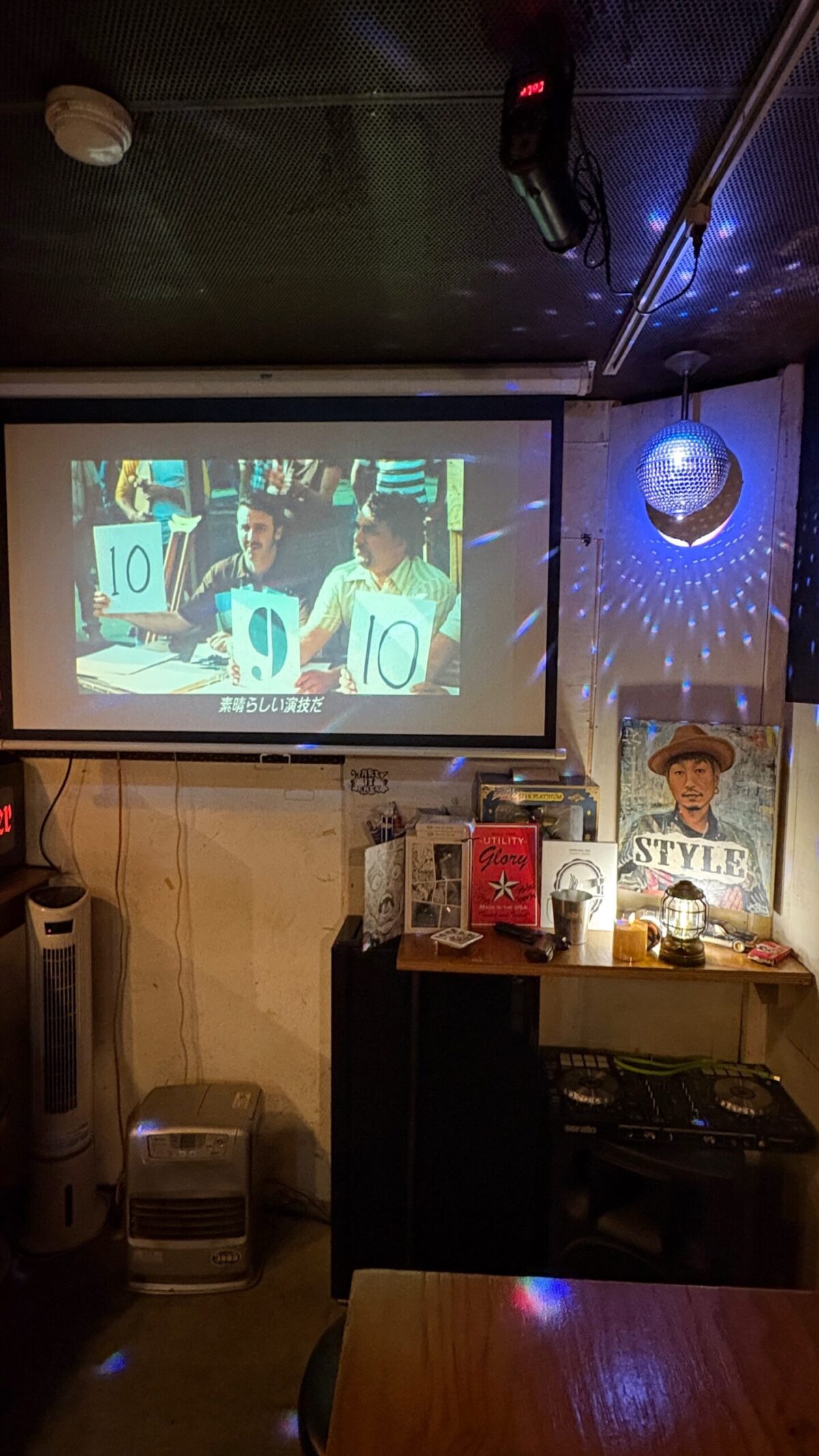 映画のシーンが映し出されたプロジェクターのスクリーンと、店主の似顔絵アートが飾られたカウンターの一角